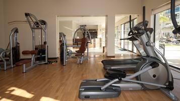 A gym with various exercise equipment, including treadmills and weight machines, with large windows providing natural light.