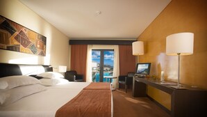 Ein Hotelzimmer mit einem Bett, einem Schreibtisch, zwei Stühlen, einem Fernseher und Blick auf die Stadt.