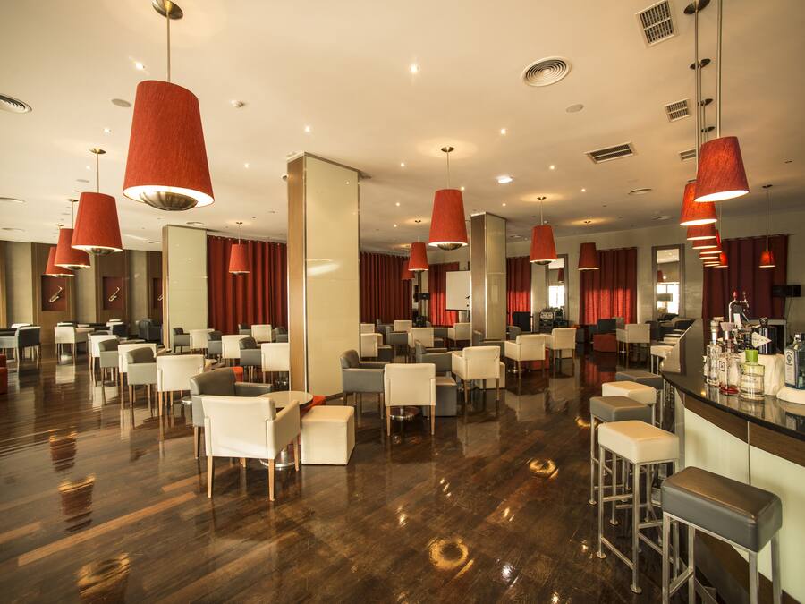 A spacious hotel lobby with multiple seating areas, a bar, and modern red pendant lighting.