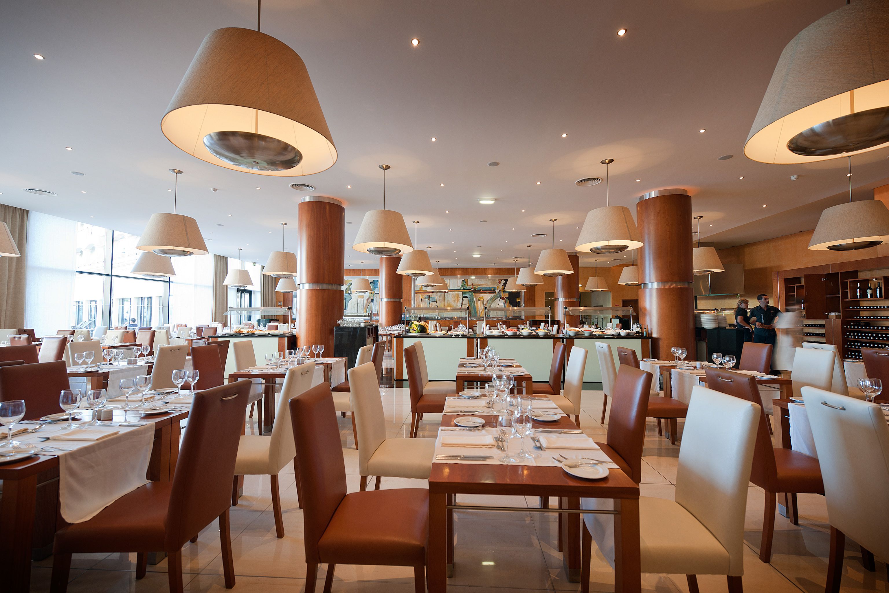 A restaurant with multiple dining tables, chairs, and hanging lamps.