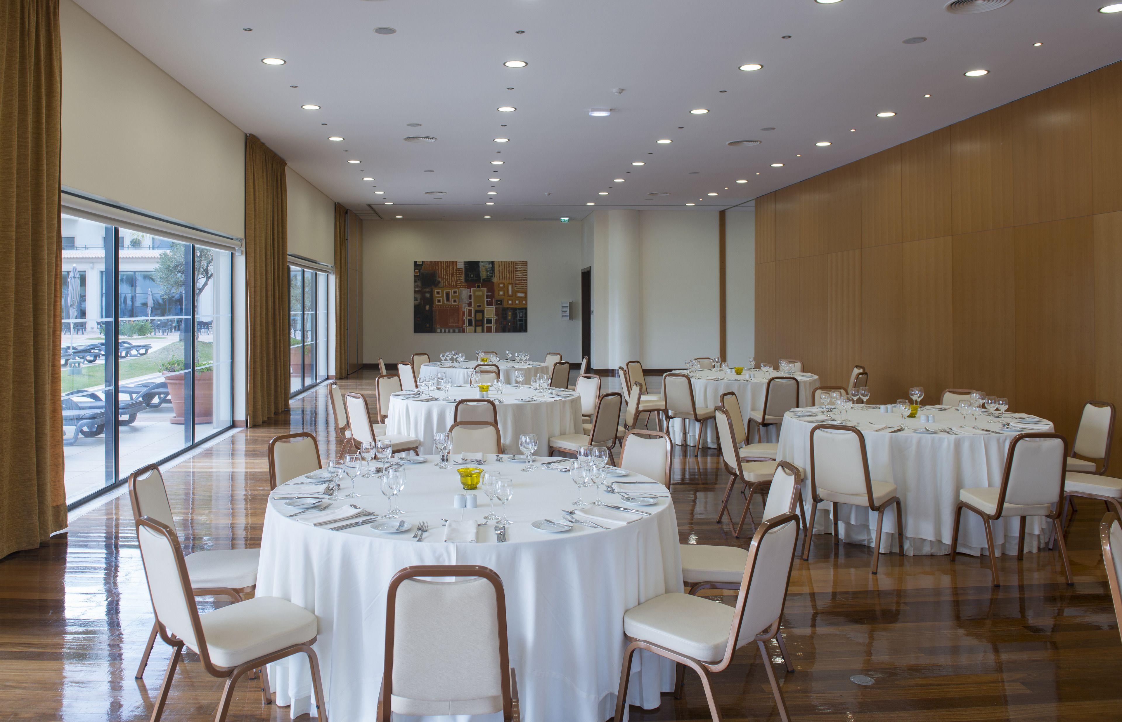 A conference room with multiple round tables set for dining, equipped with chairs and table settings.
