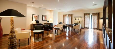 A spacious hotel lobby with a wooden floor, multiple seating areas, and a reception desk.