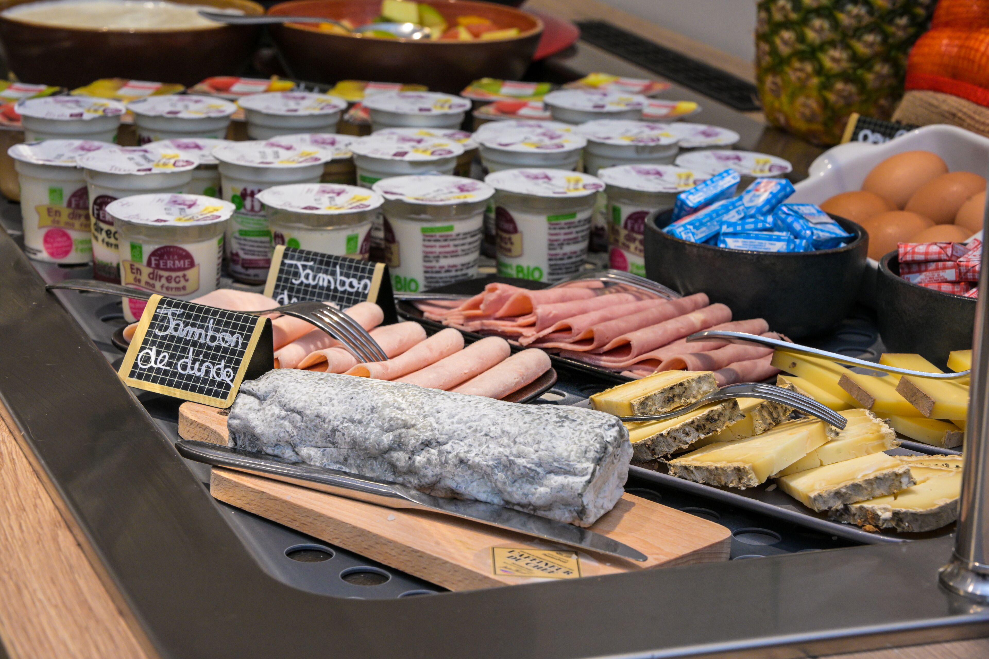 A buffet with various food items including meats, cheeses, and yogurt containers.