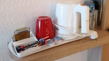 A kitchen counter with a coffee maker, a red mug, a tray with a box of tissues, and a water bottle.