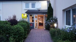 A hotel entrance with a glass door, a sign for 'Logis', and a brick pathway leading to the entrance.