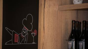 A chalkboard with a chef illustration, a teapot, and wine bottles on shelves.