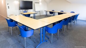 A conference room with a long table, blue chairs, a whiteboard, and a TV screen.