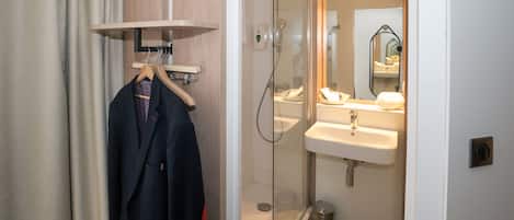 A modern bathroom with a glass shower enclosure, a wooden vanity, and a hanging coat rack.