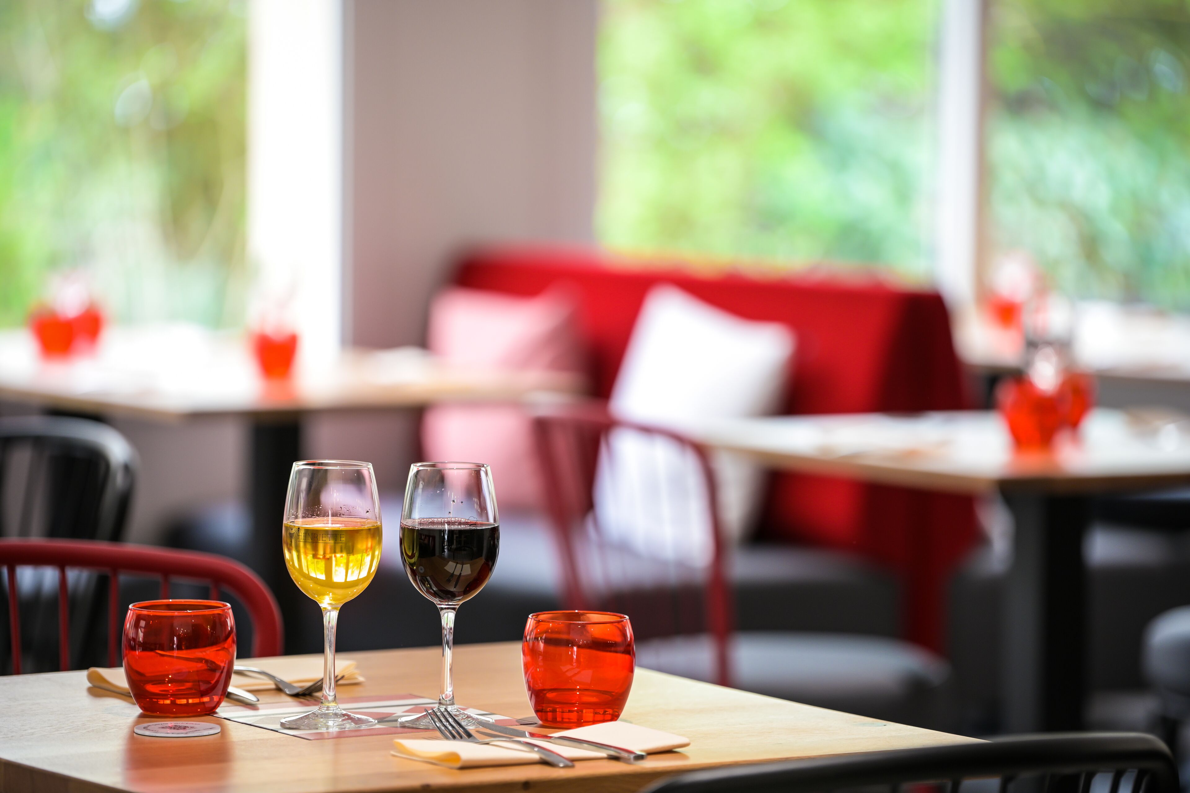 Una mesa de comedor con dos copas de vino y una copa roja, dispuesta con cubiertos y una servilleta.