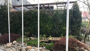 A landscaped garden with a variety of plants and rocks, a wooden bench, and a pergola structure. - Hotel Ciudad De Lugo (Lugo)