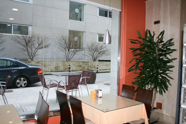 Un área de estar interior con una mesa de vidrio, sillas de metal y una planta en maceta.