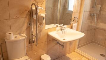 A bathroom with a toilet, sink, mirror, and shower.
