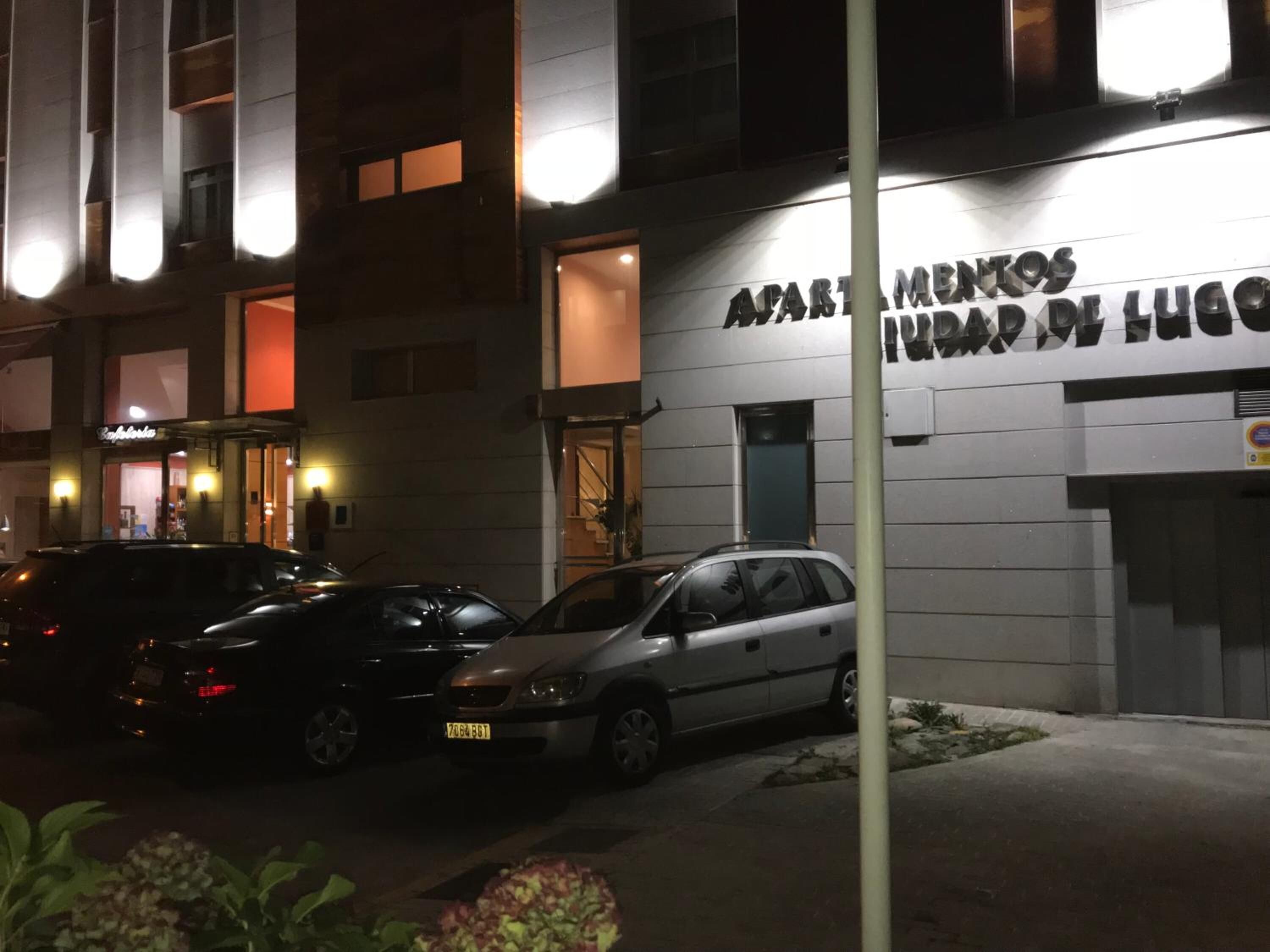A building with a sign reading "Apartamentos Incondicional de Lugar." There are cars parked in front, and the building has multiple windows and balconies.