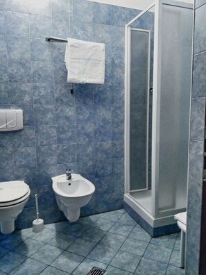 Un baño con inodoro, bidé, lavamanos y cabina de ducha con mampara de vidrio.