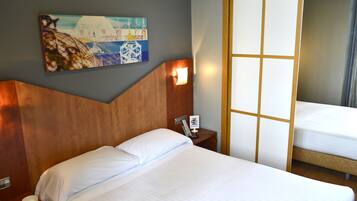 Habitación de hotel con una cama grande, una mesita de noche con lámpara, un cuadro en la pared y una puerta corredera.