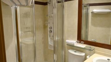 A glass-enclosed shower with a glass shelf above the toilet, a white sink, and a mirror above the sink.