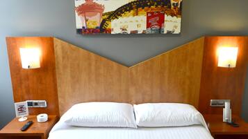 Una habitación de hotel con una cama, dos mesitas de noche, una obra de arte colgada en la pared y una lámpara de pared.