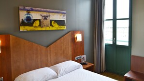 Una habitación de hotel con una cama, un cuadro en la pared, una mesita de noche con un letrero y una puerta verde.