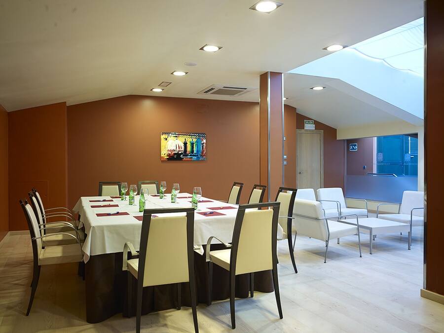 Un comedor con una mesa larga dispuesta para seis personas, rodeada de sillas. Se observa un amplio ventanal que proporciona luz natural, y un colorido cuadro en la pared.