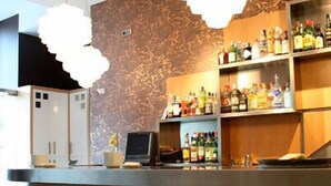 Una recepción moderna con un papel tapiz estampado, una cafetera y una zona de bar con varias botellas.