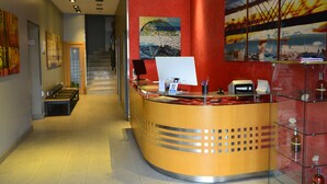 Zona de recepción de un hotel con un mostrador curvo, una escalera al fondo y obras de arte en las paredes.