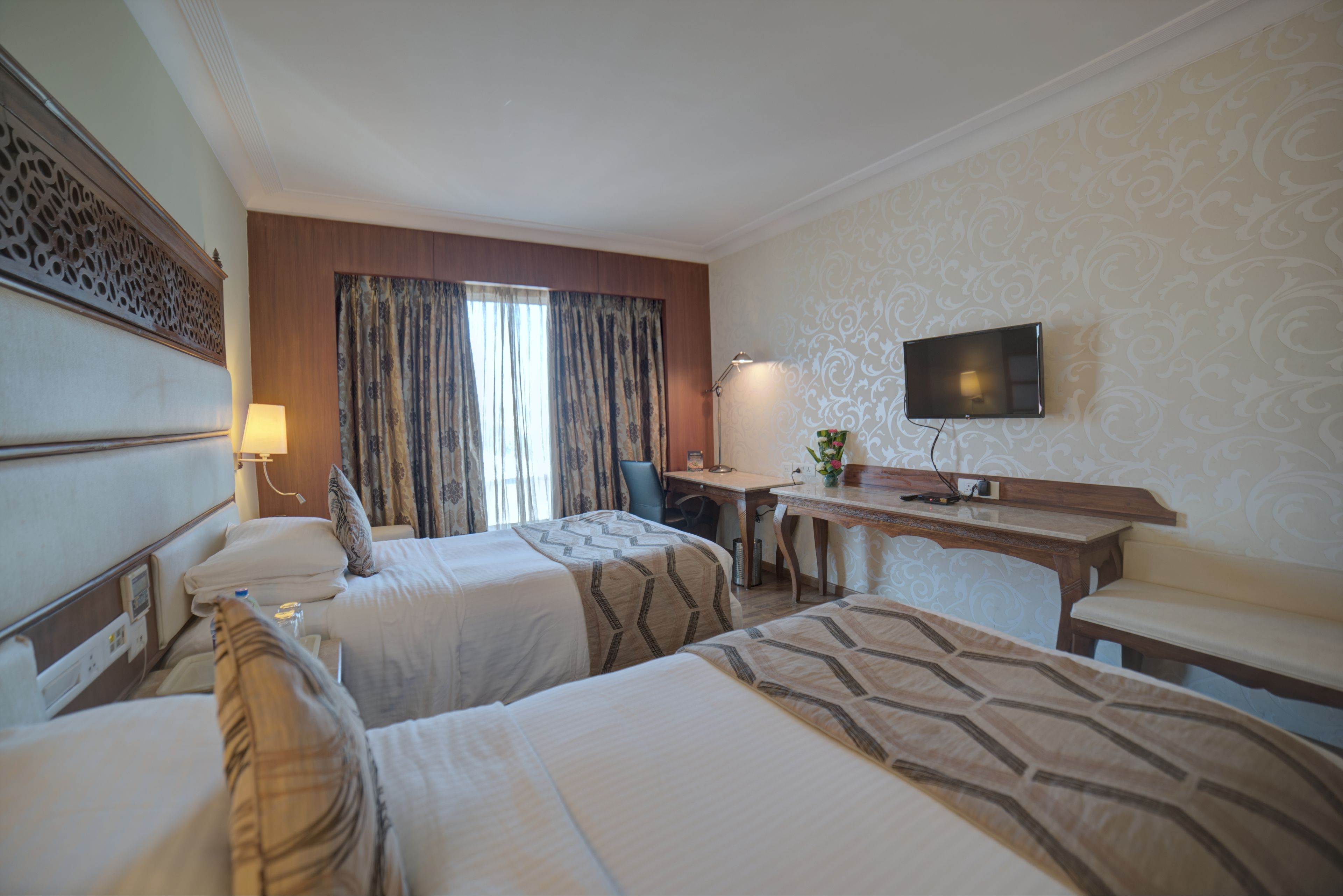 A hotel room with two beds, a desk, a chair, a TV, and a window with curtains.
