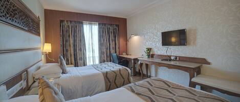 A hotel room with two beds, a desk, a chair, a TV, and a window with curtains.