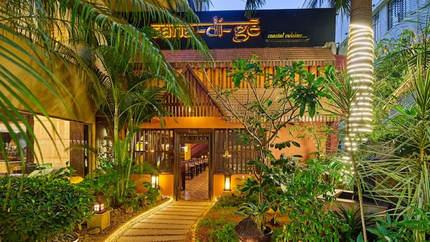 A coastal restaurant with a tropical garden entrance, a staircase leading to the dining area, and a sign indicating coastal cuisine. - Goldfinch Hotel Bangalore (Bengaluru)