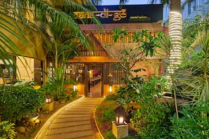 Un restaurante costero con un jardín tropical en la entrada, una escalera que lleva al comedor y un letrero que indica cocina de mariscos.