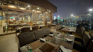 An outdoor dining area with tables and chairs, large windows, and a view of the city at night. - Goldfinch Hotel Bangalore (Bengaluru)