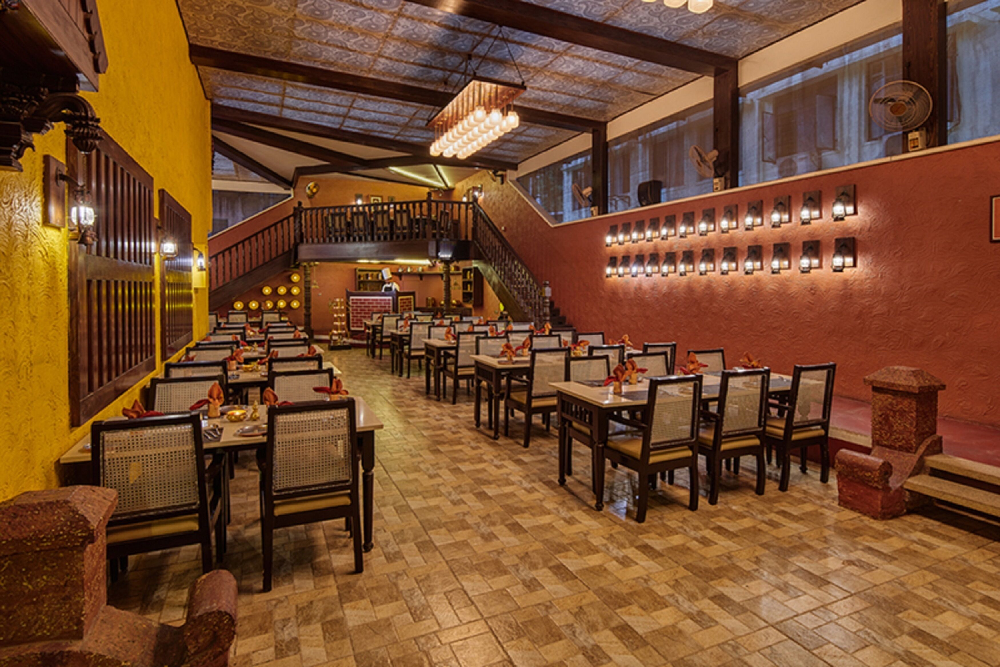 Ein Restaurant mit Schachbrettmuster-Boden, Holztischen und -stühlen, einer Treppe und Wandleuchten.