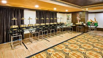 Un salón de banquetes con varias mesas y sillas, una alfombra estampada y una mesa de buffet.