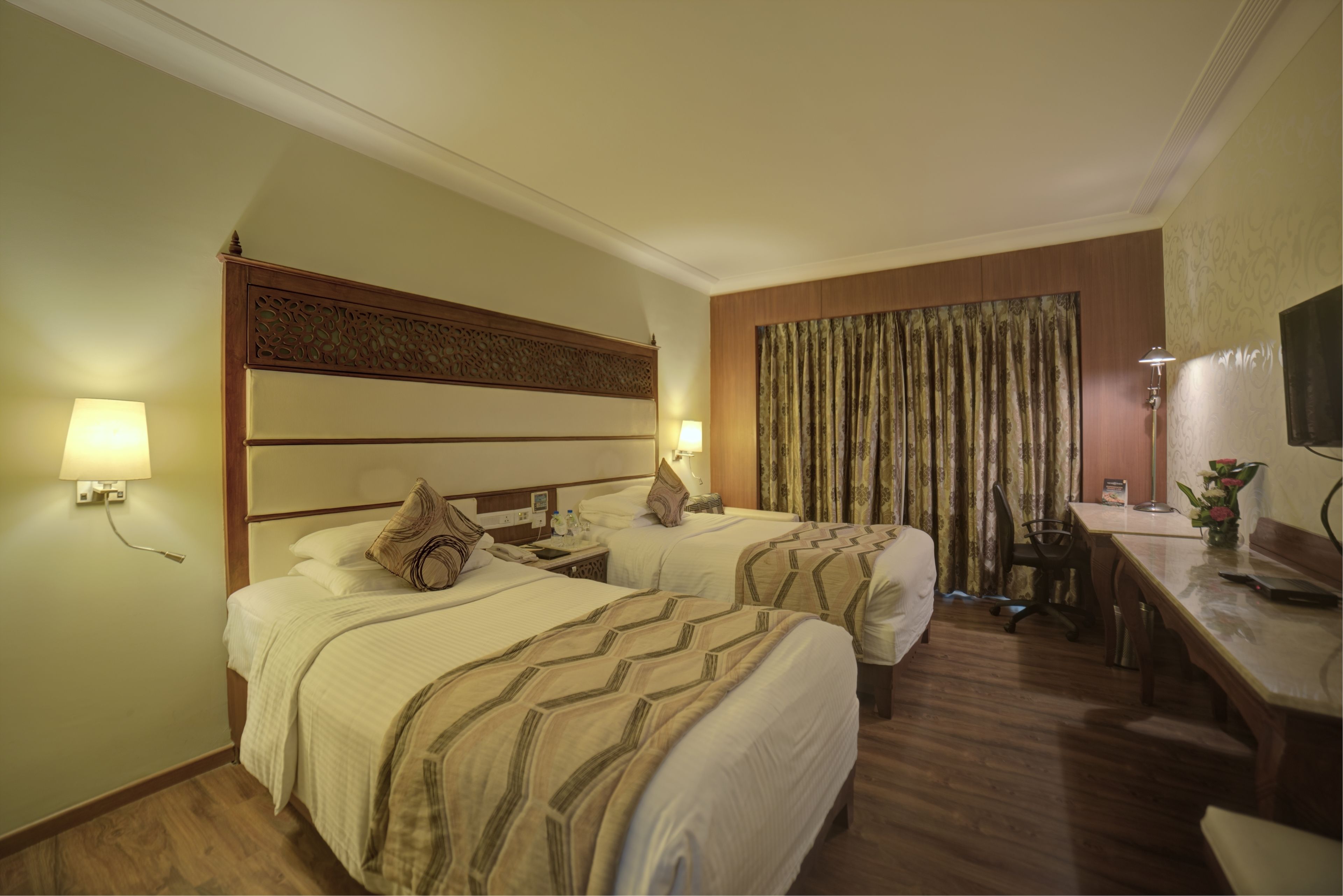 A hotel room with two beds, a desk, a chair, and a television.