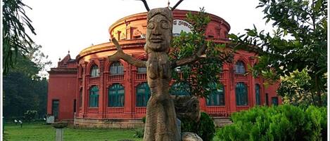 A building with a circular facade and a sculpture of a tree with a human figure.