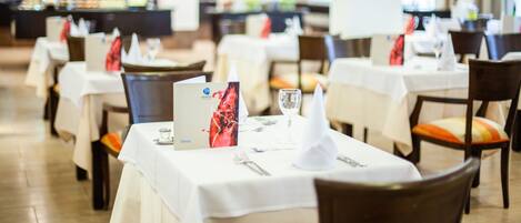 A restaurant with round tables set for dining, white tablecloths, and menus.