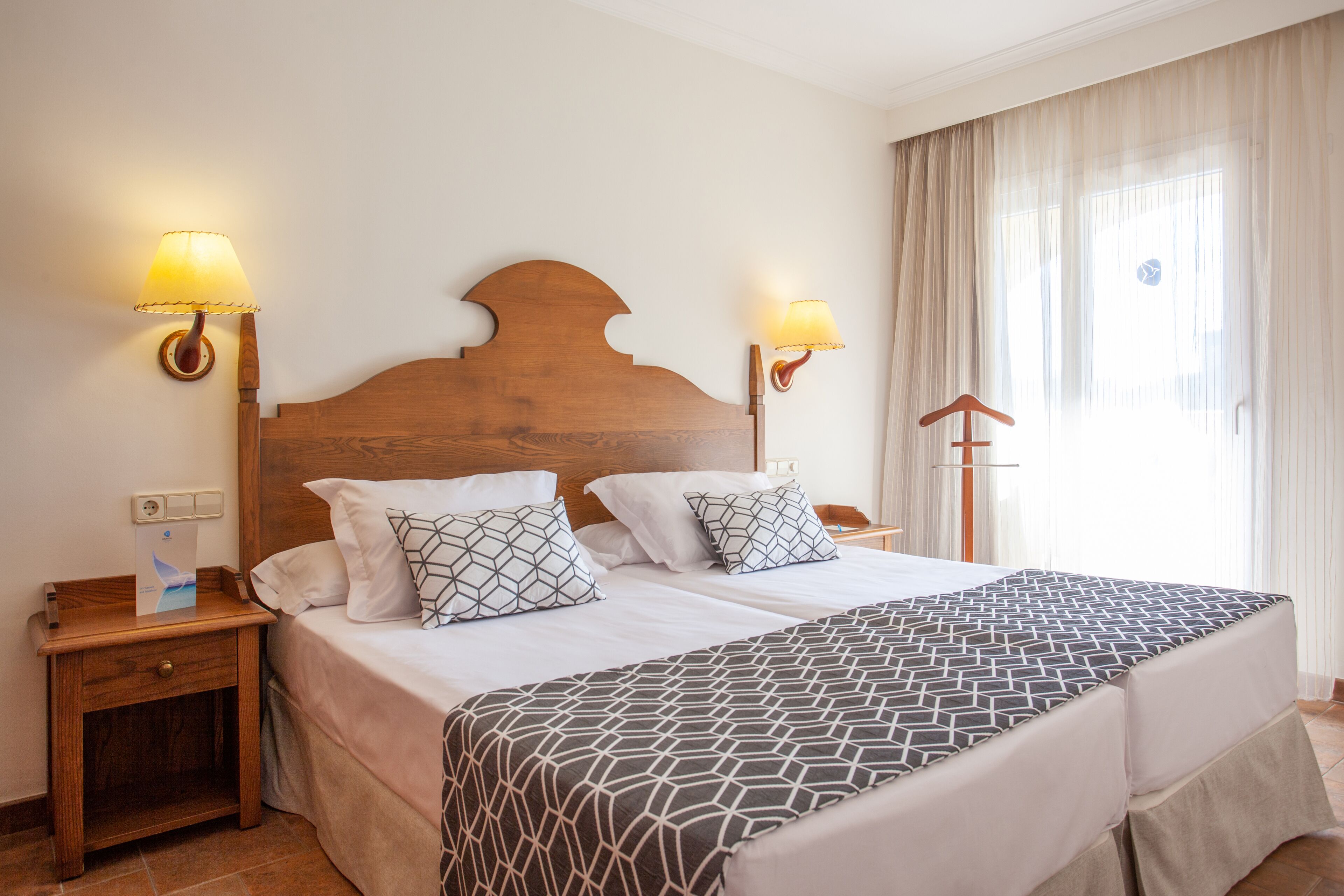 A double bed with a geometric patterned bedspread, two bedside lamps, and a wooden headboard.
