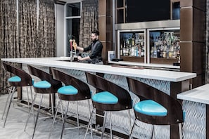 A bar area with a bartender, bar stools, and a display of liquor bottles.