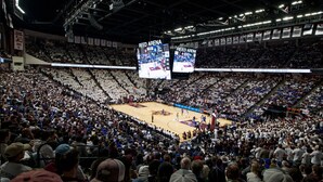 A large indoor arena with multiple tiers of seating, digital scoreboards, and a basketball court.