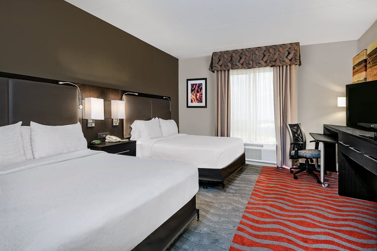 A hotel room with two beds, a desk, a chair, a TV, and a window with curtains.