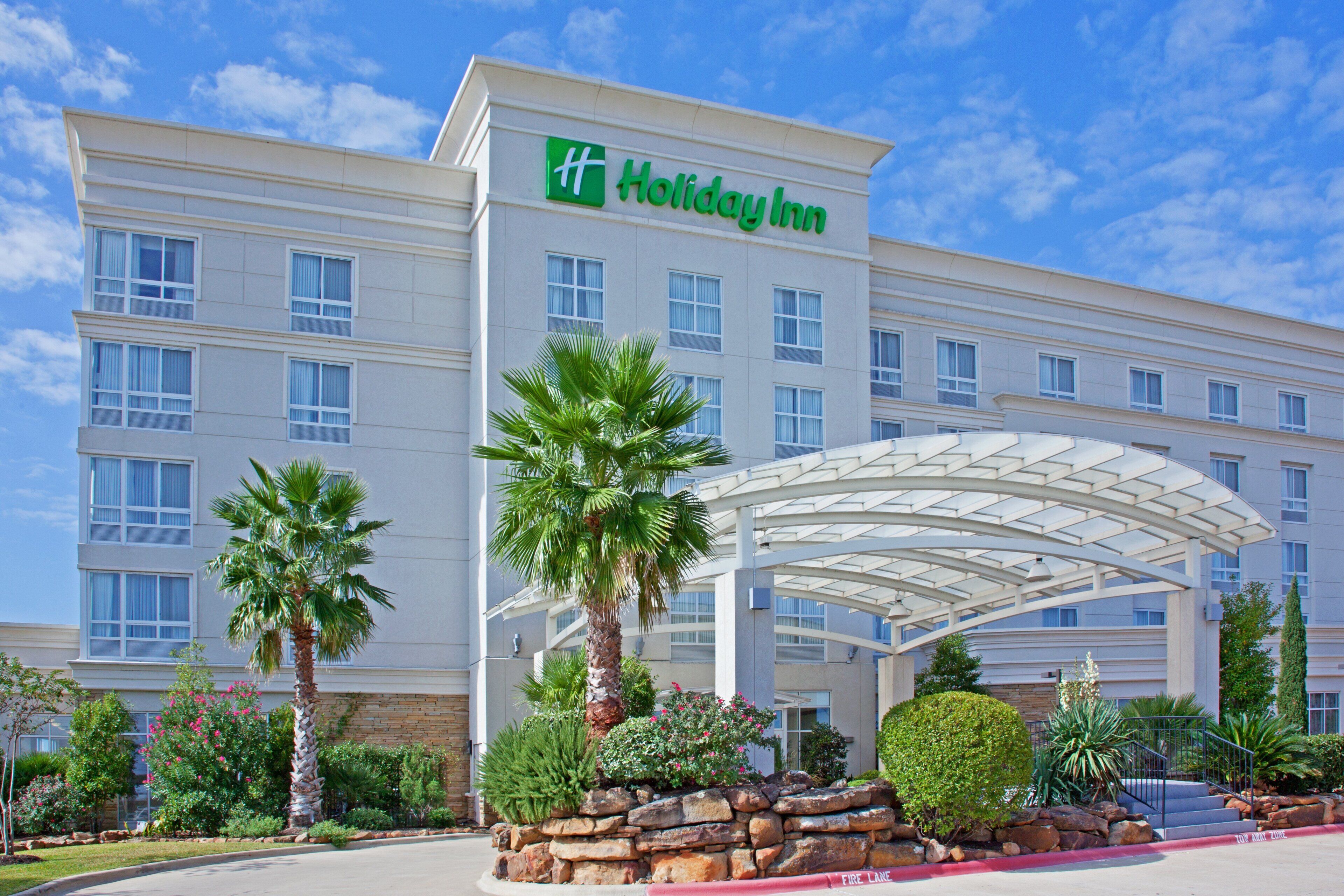 A Holiday Inn hotel with a covered entrance, palm trees, and a stone wall.
