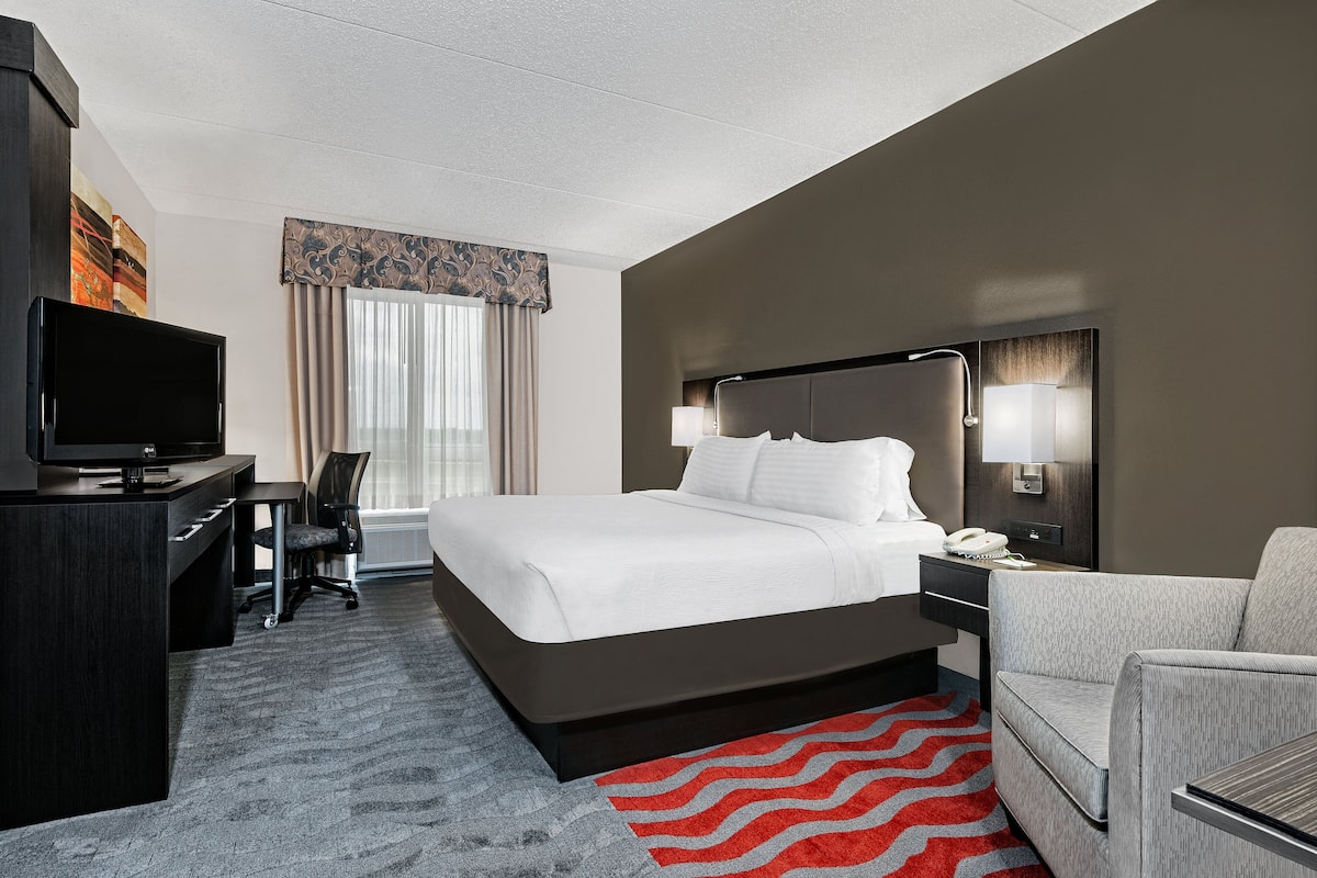 A hotel room with a bed, desk, chair, and a television.