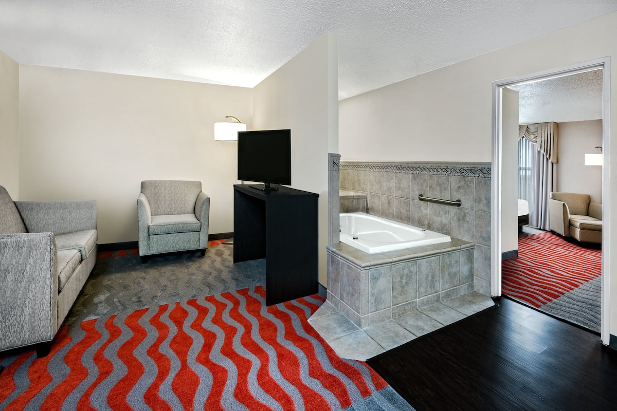 A modern hotel bathroom with a bathtub, a shower area, and a seating area with two chairs.