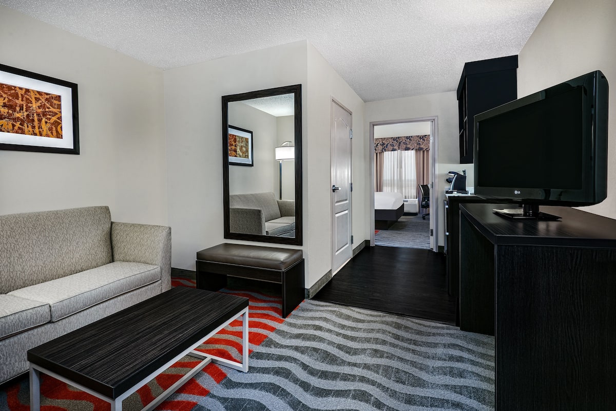 A hotel room with a sofa, a coffee table, a TV, a mirror, and a door leading to a bathroom.