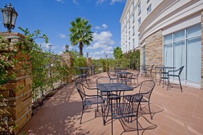 An outdoor patio with tables and chairs, stone walls, and a palm tree.