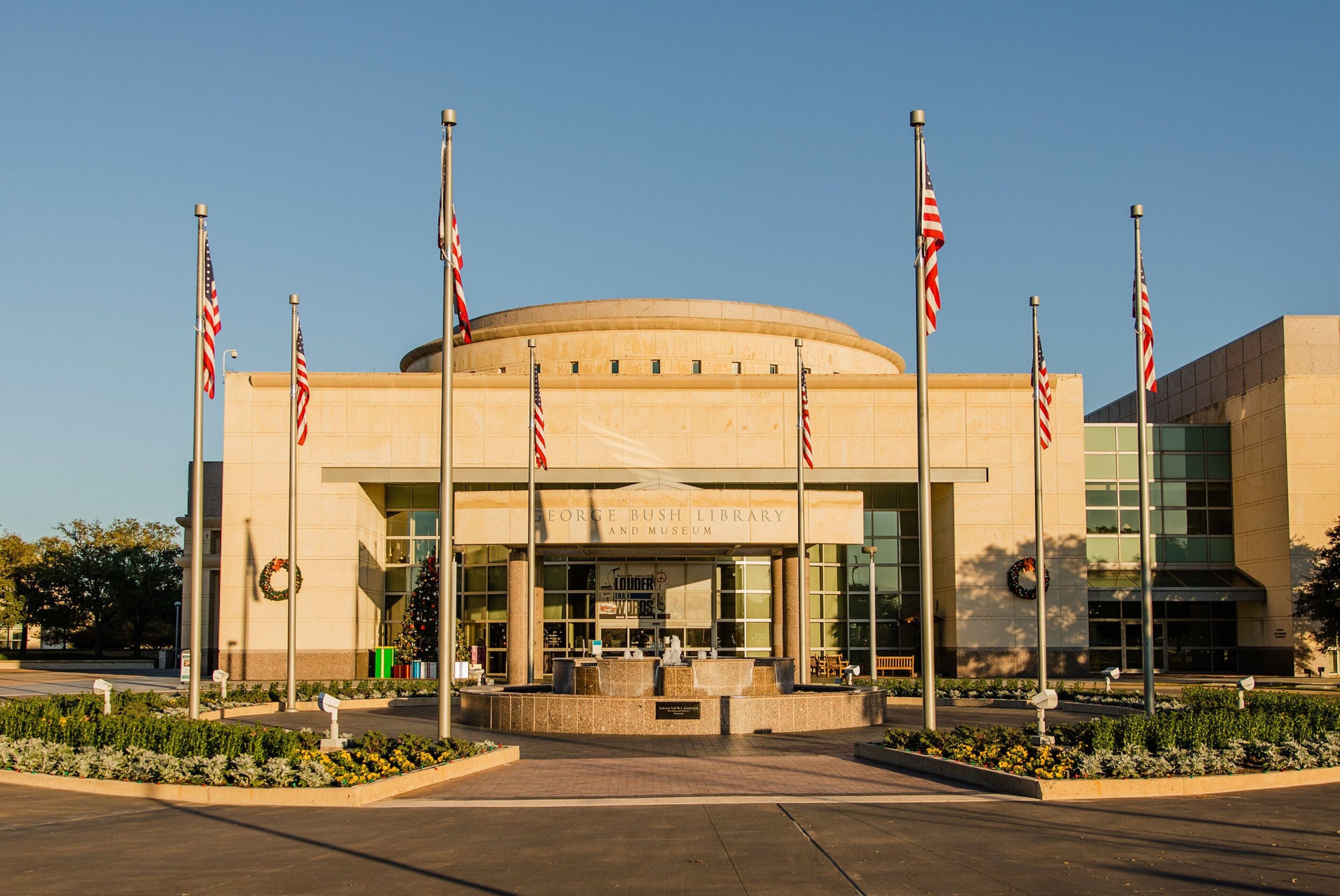 El exterior de la Biblioteca y Museo George Bush, con una entrada circular, banderas estadounidenses y un adorno navideño.