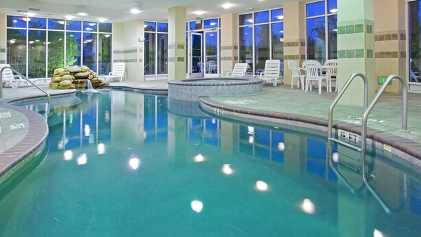 An indoor swimming pool with clear water, surrounded by white lounge chairs and a stone wall.
