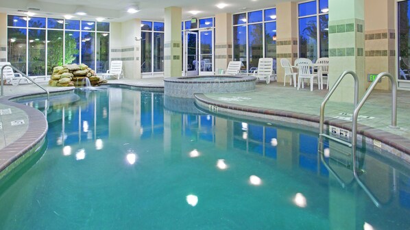 An indoor swimming pool with clear water, surrounded by white lounge chairs and a stone wall.