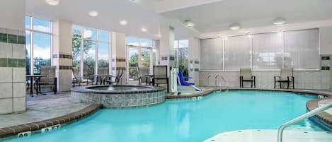 Una piscina interior con jacuzzi, zona de estar y amplias ventanas.