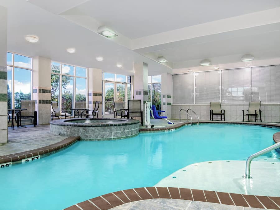 An indoor swimming pool with a hot tub, seating area, and large windows.