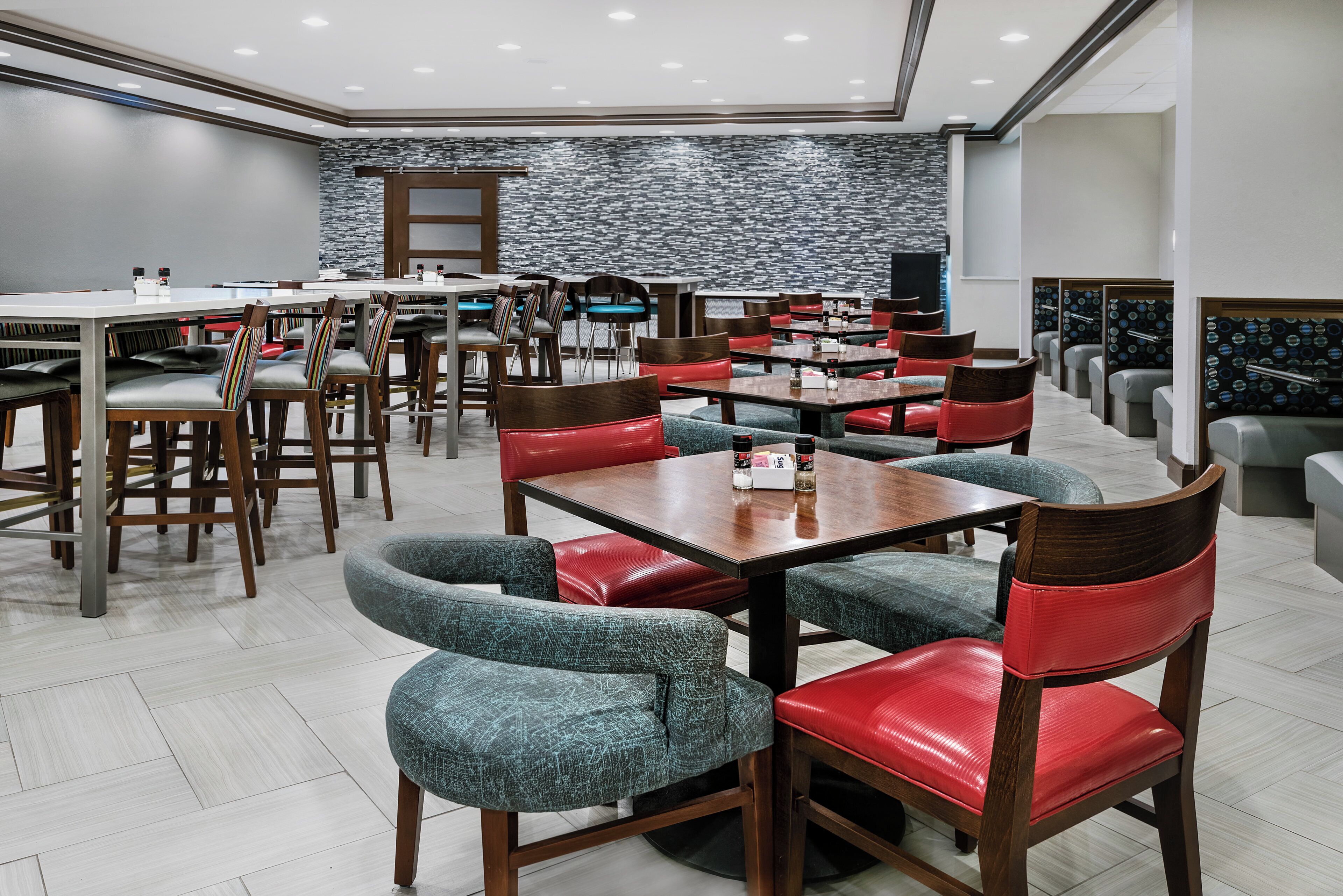 A modern restaurant interior with multiple dining tables and chairs, a patterned wall, and a clean, well-lit environment.